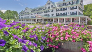 A large, multi-story hotel with a green roof and white exterior. It features a covered front porch with hanging flower baskets. - Eagle Mountain House & Golf Club (Jackson)