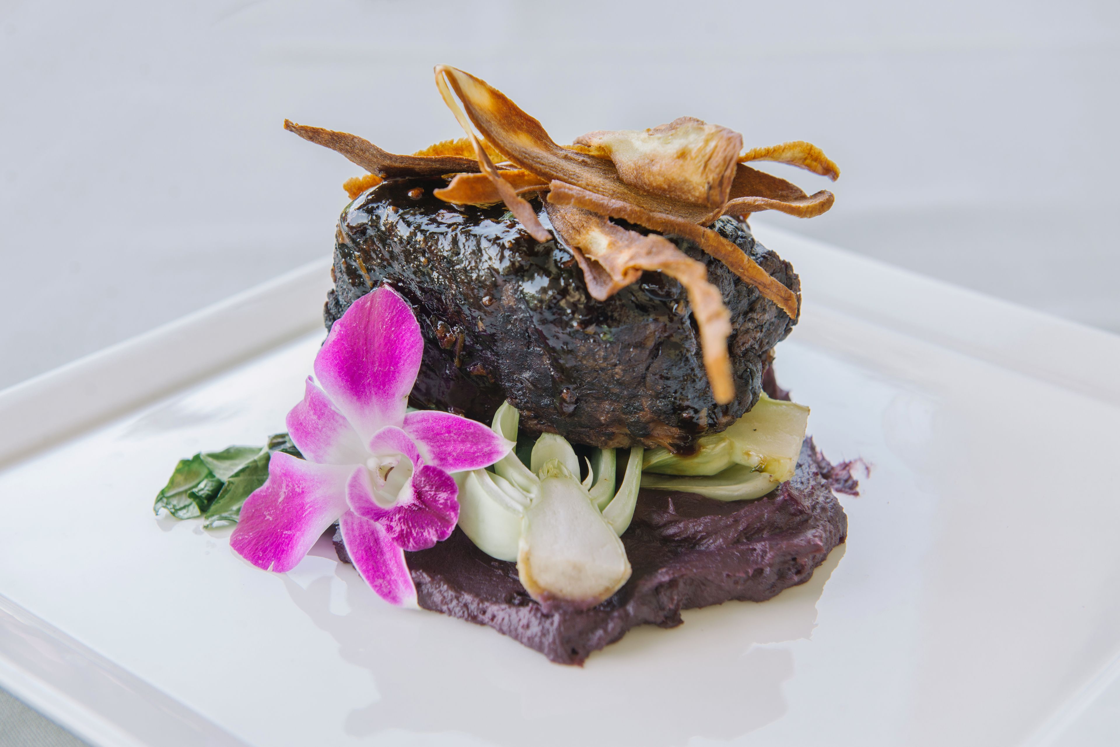Un plato con base oscura y texturizada, adornado con carne en lonjas finas y una flor.