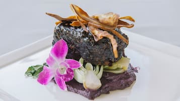 Un plato con base oscura y texturizada, adornado con carne en lonjas finas y una flor.