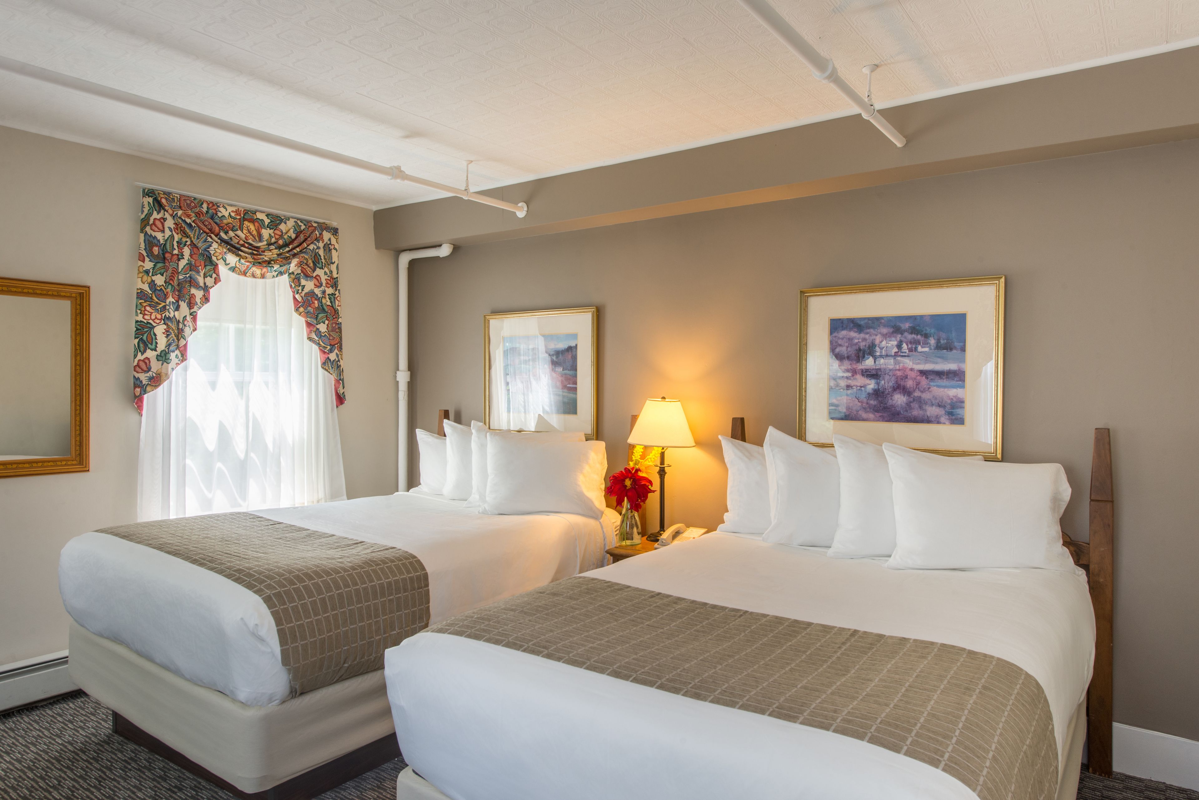 Habitación de hotel con dos camas, una mesita de noche con lámpara y cuadros en las paredes.