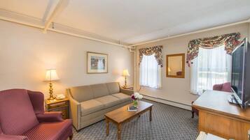 A hotel room with a sofa, armchair, coffee table, TV, and a desk.