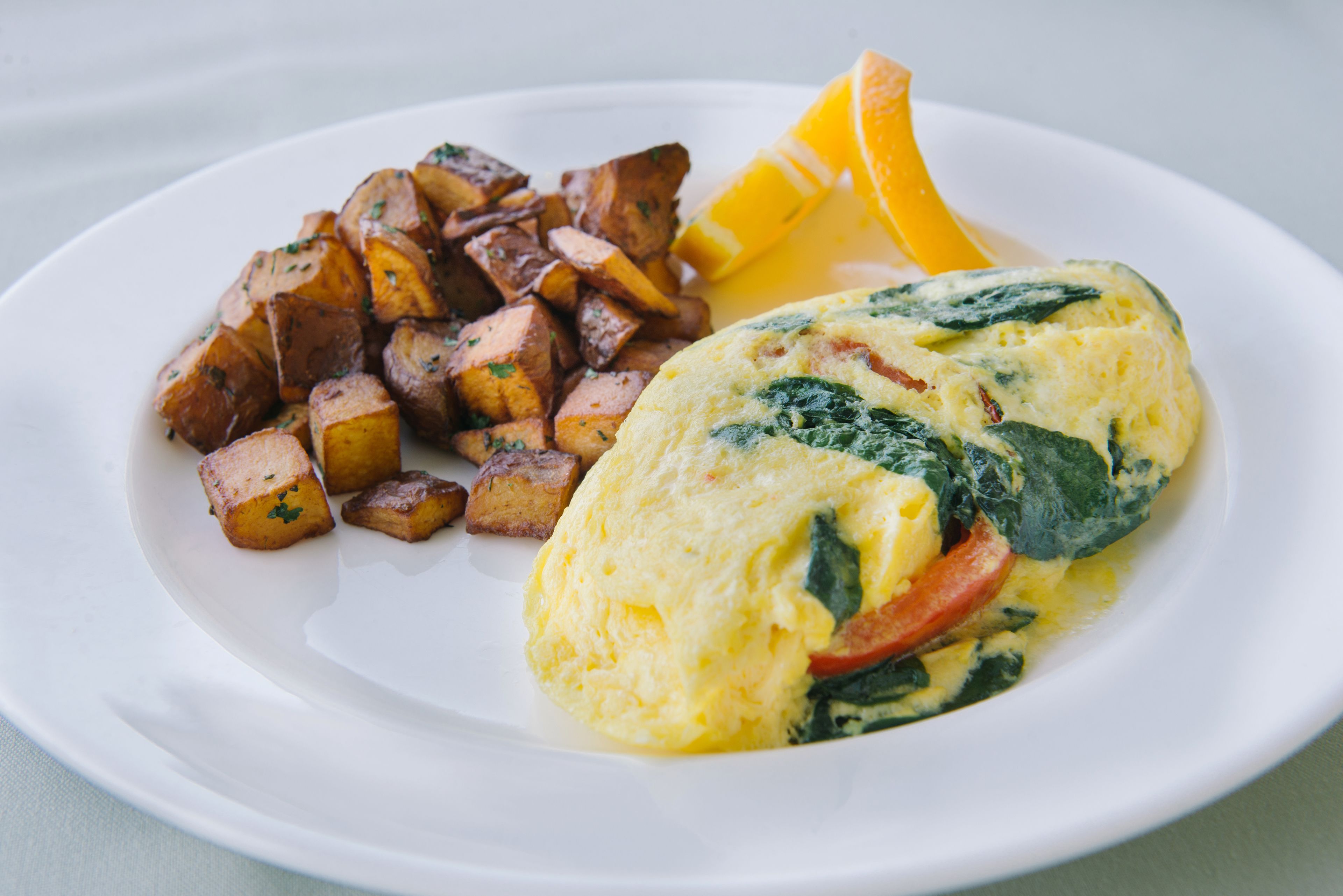 A plate with an omelette, roasted potatoes, and a slice of orange.