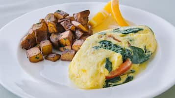A plate with an omelette, roasted potatoes, and a slice of orange.