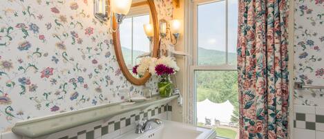 A bathroom with a floral wallpaper, a large mirror, a sink, and a window with curtains.