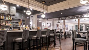 A bar area with multiple stools, a bar counter, and shelves stocked with bottles and glasses. - Eagle Mountain House & Golf Club (Jackson)