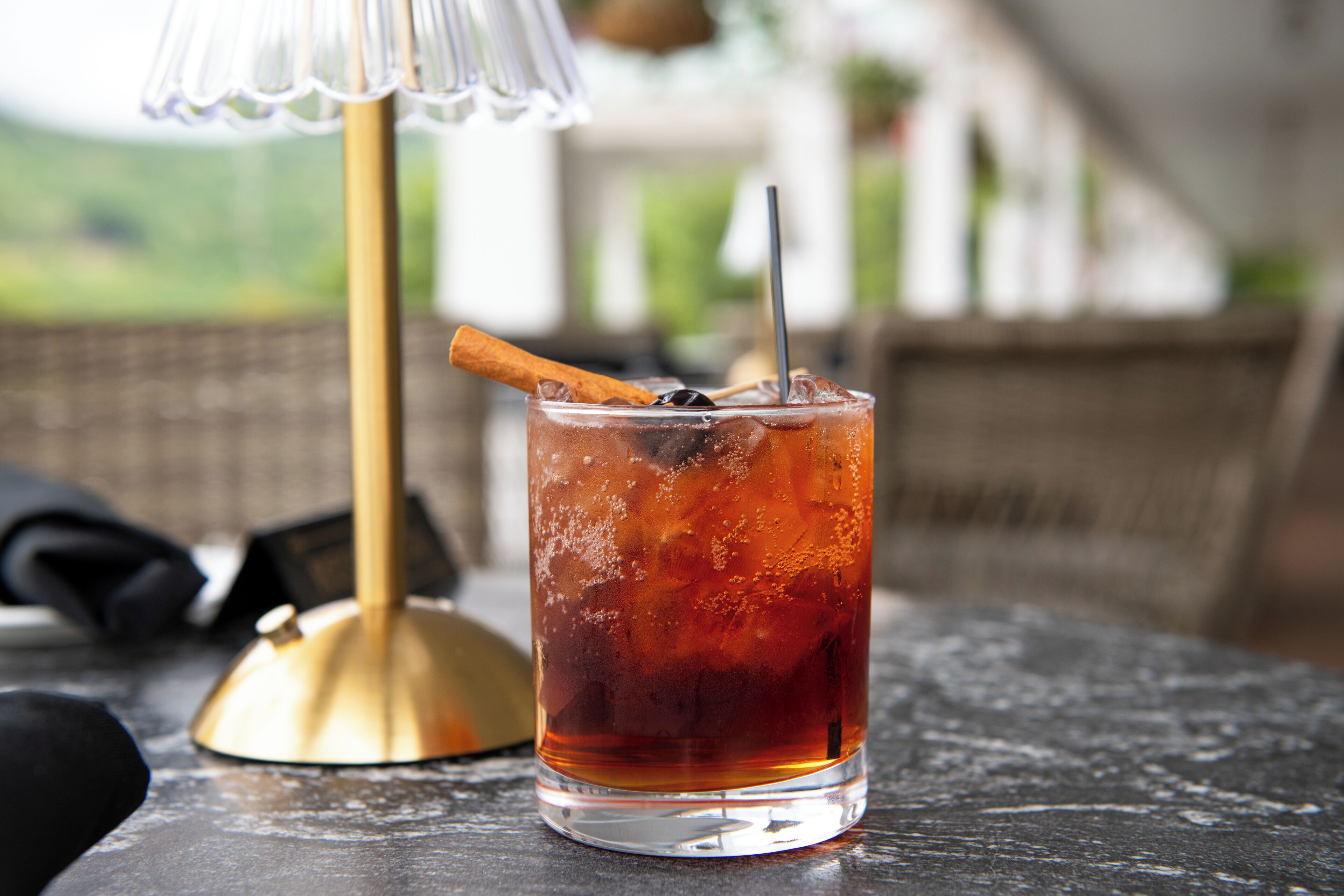 A glass of iced tea with a cinnamon stick and a straw on a table.