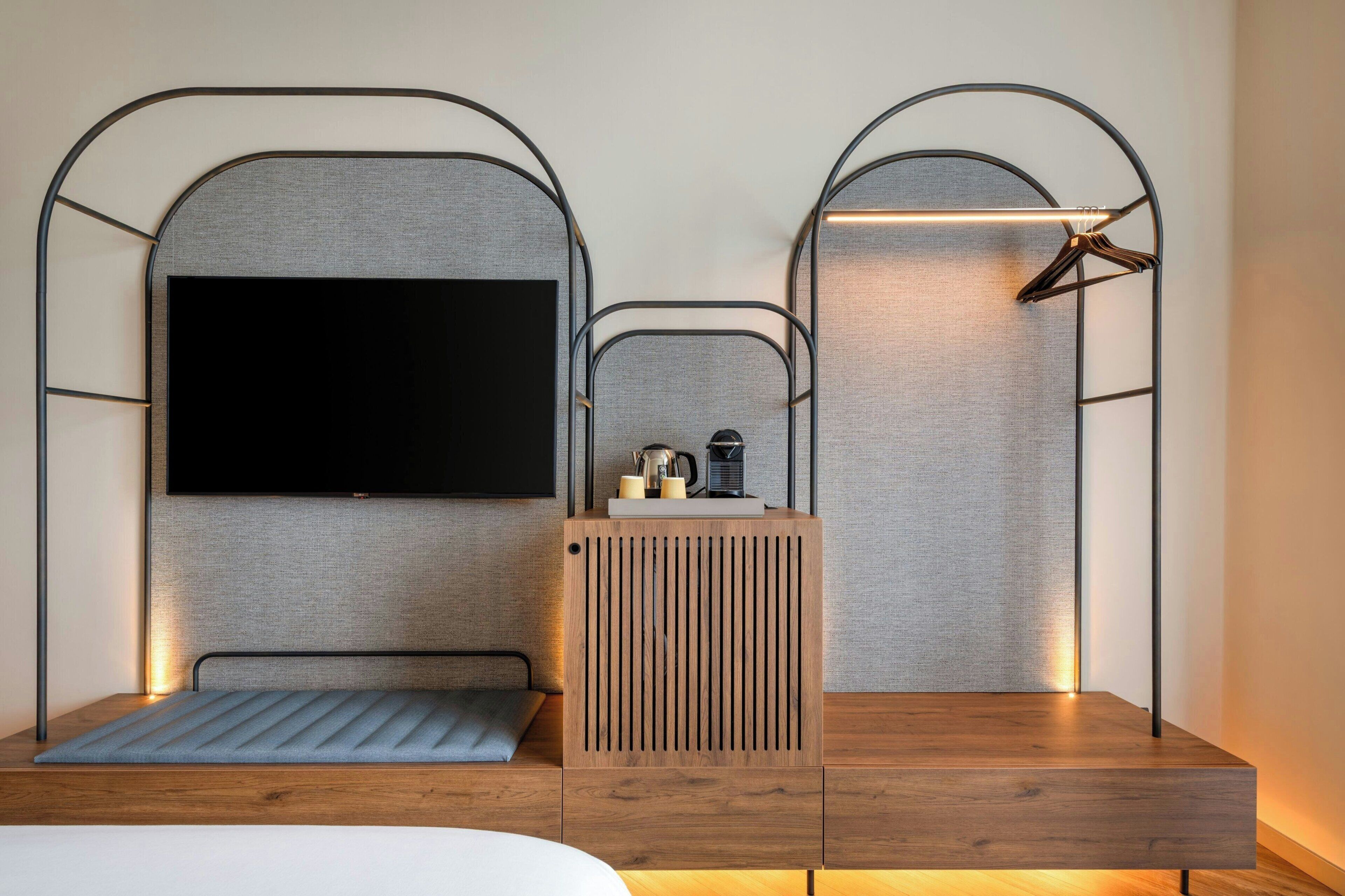 Un dormitorio moderno con cama, televisor, mesita de madera y lámpara colgante.