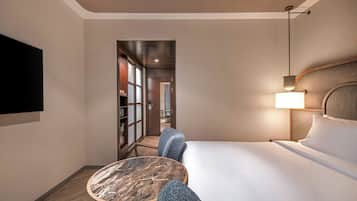 Habitación de hotel con cama, escritorio y silla, televisor montado en la pared y lámpara en la mesita de noche.