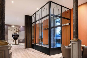 Un hall d’entrée moderne avec une cloison en verre, des panneaux en bois et un grand vase posé sur une table.