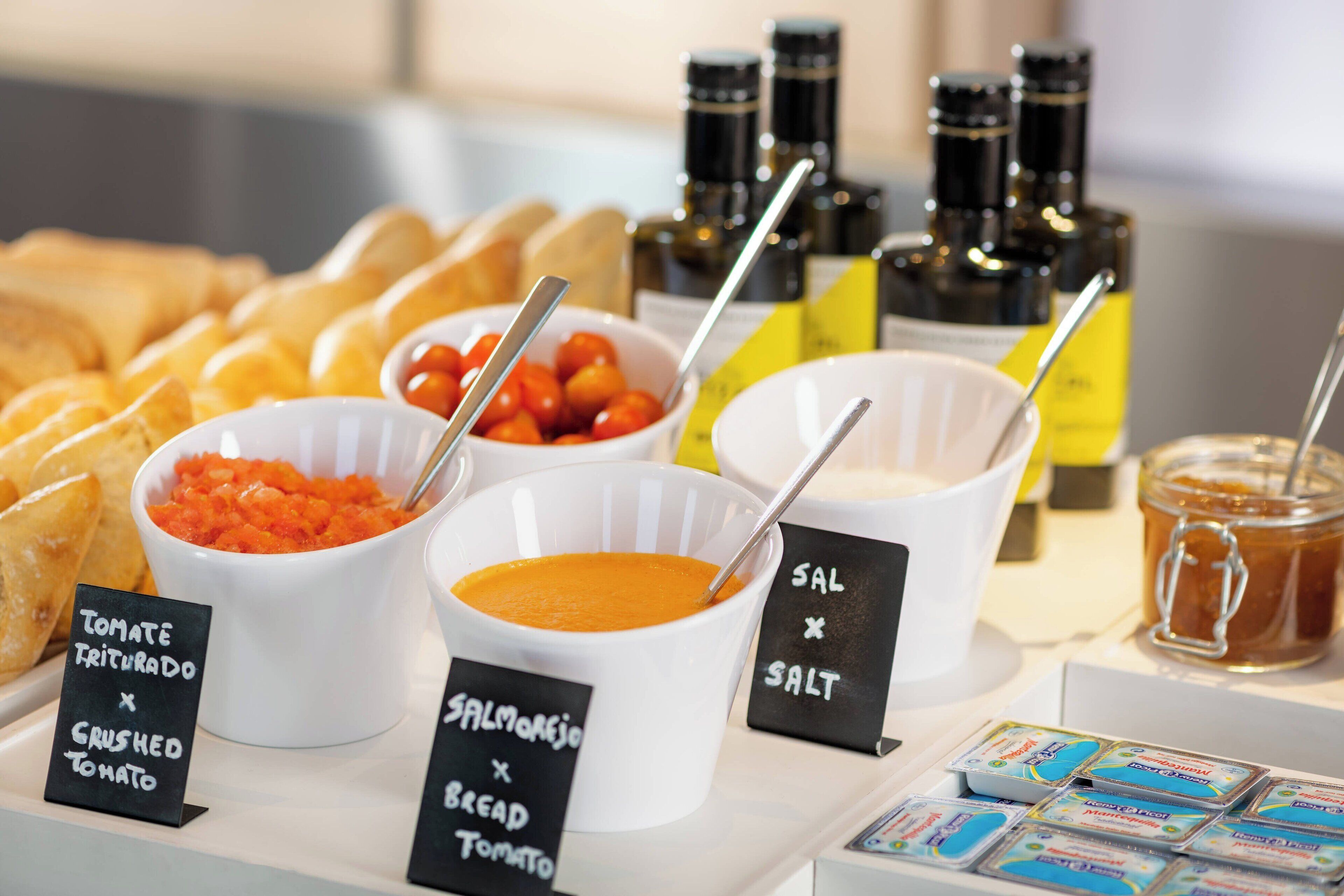 A buffet table with various food items and condiments, including bowls of tomato sauce, salmon, and bread, along with salt and pepper shakers.