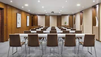 Uma sala de conferência com uma mesa comprida e várias cadeiras, painéis de madeira nas paredes e um projetor no teto.