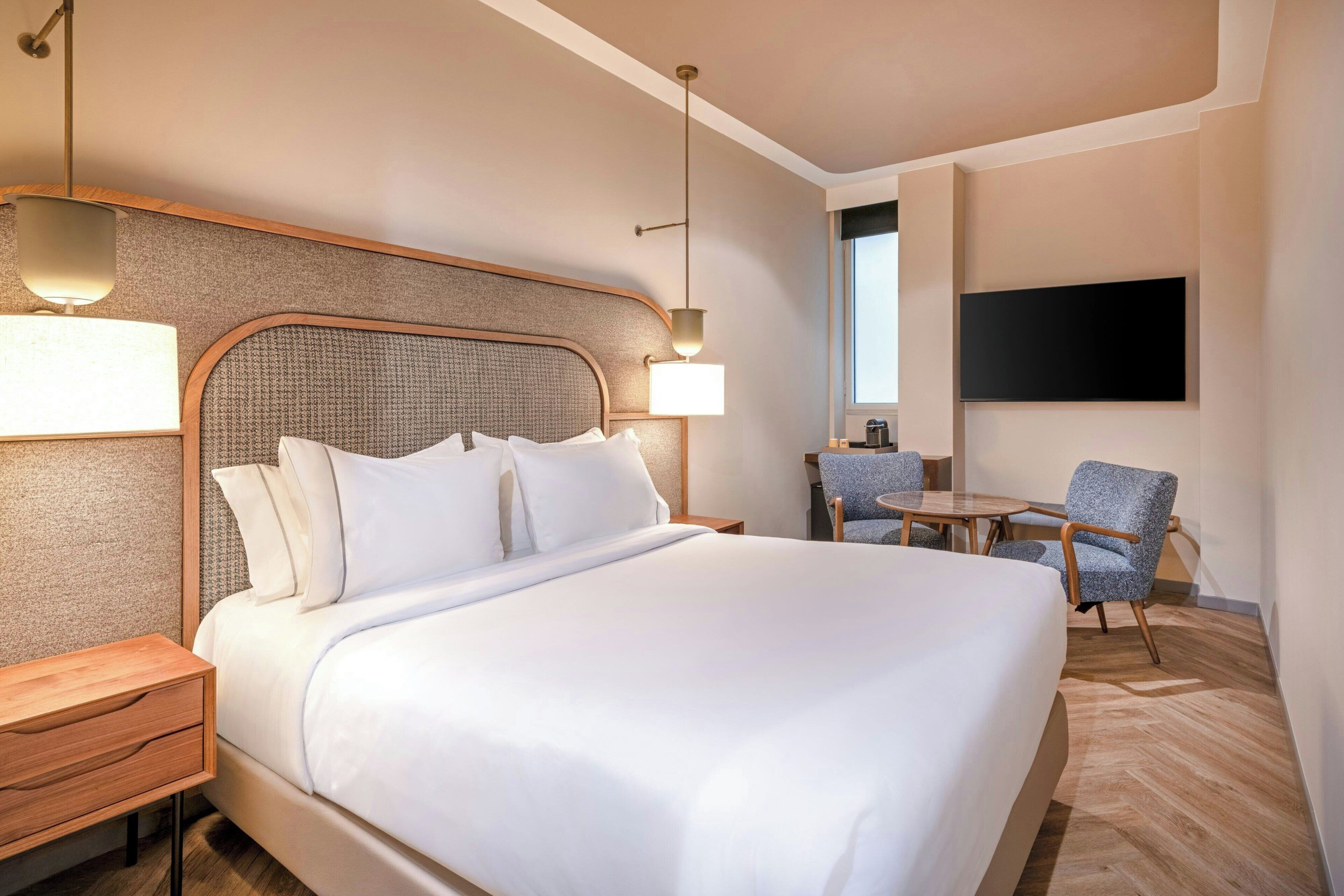 Habitación de hotel con una cama grande, mesitas de noche, un escritorio, una silla y un televisor montado en la pared.