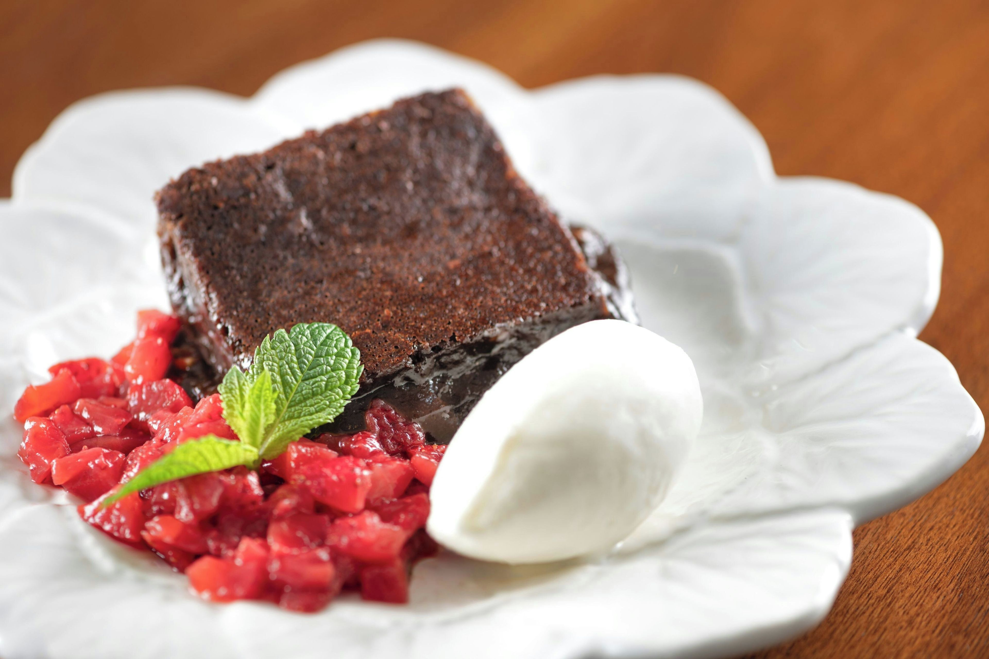 Een dessert met een vierkant stuk cake, een bolletje ijs en een fruitcompote op een wit bord.