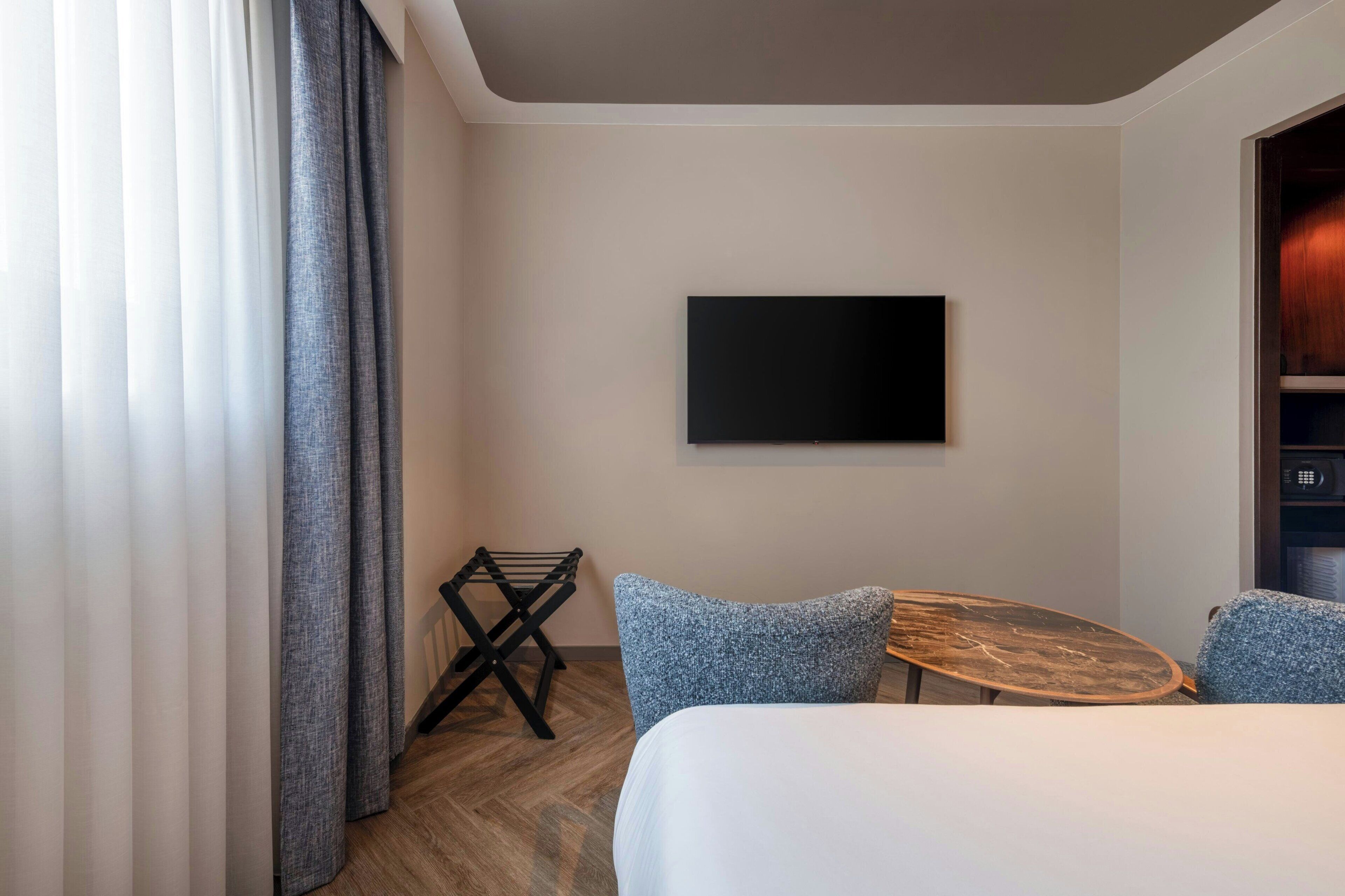 Una habitación de hotel con una cama, un televisor fijado a la pared, una mesita y una silla.