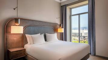 Een hotelkamer met een groot bed, twee bedlampen, een nachtkastje en een raam met uitzicht op gebouwen.