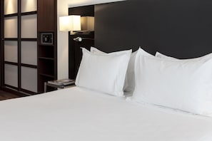 A hotel room with a neatly made bed, a bedside table with a lamp, and a wall-mounted safe. - AC Hotel Palacio Universal by Marriott (Vigo)