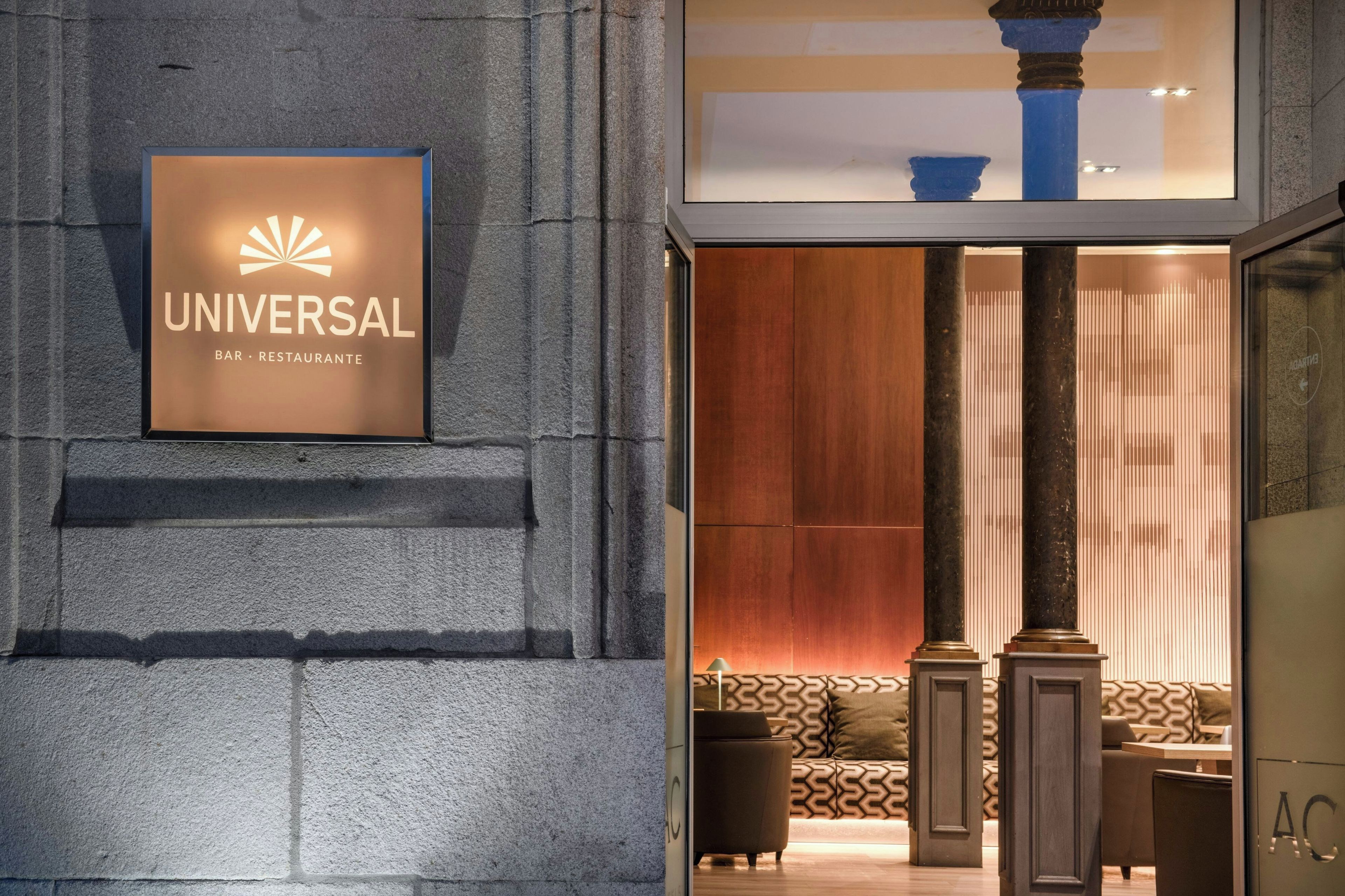 A hotel entrance with a sign reading 'UNIVERSAL BAR RESTAURANTE' and a modern interior with a sofa and a lamp.