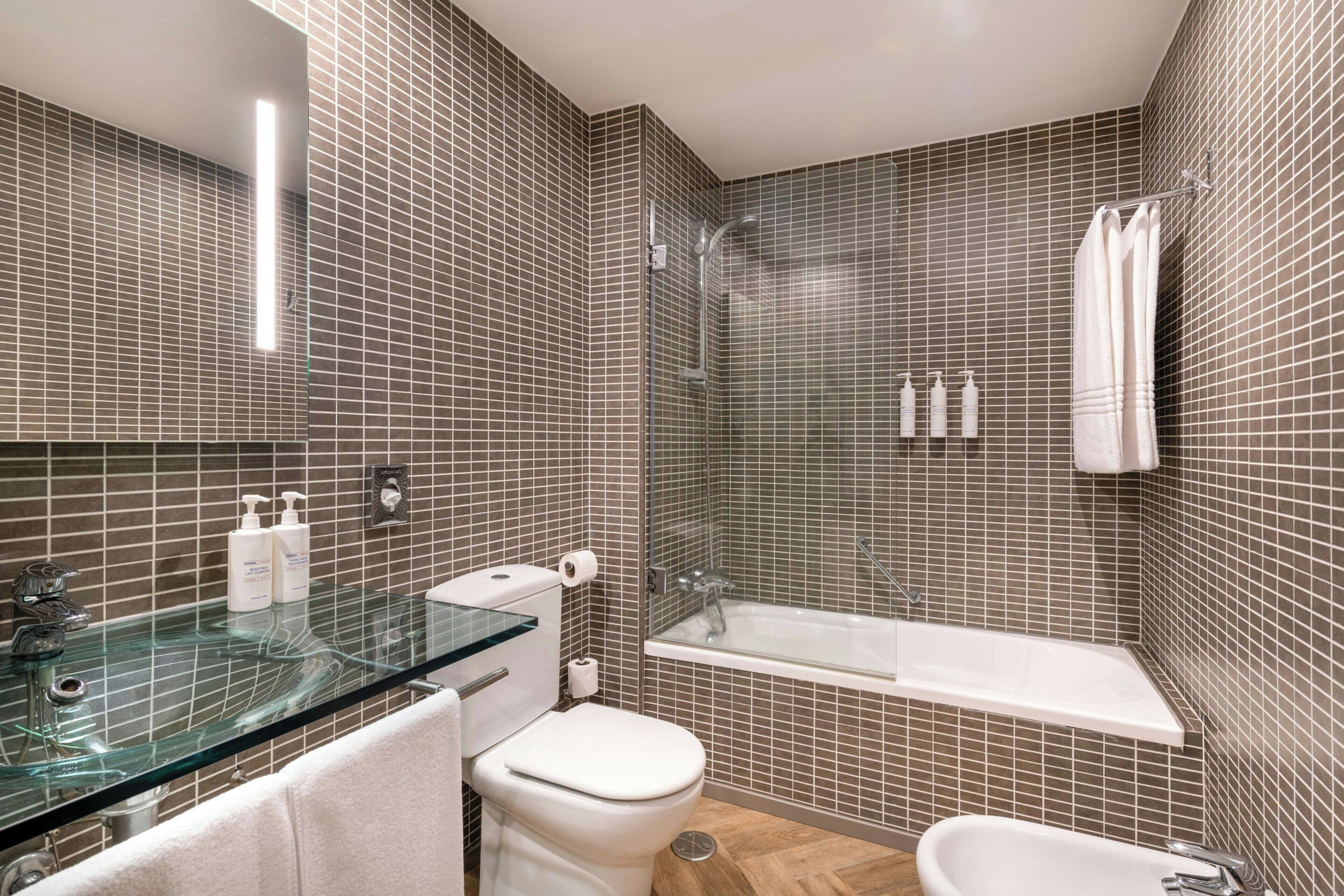 Een moderne badkamer met een douchecabine van glas, een wit toilet en een bad.