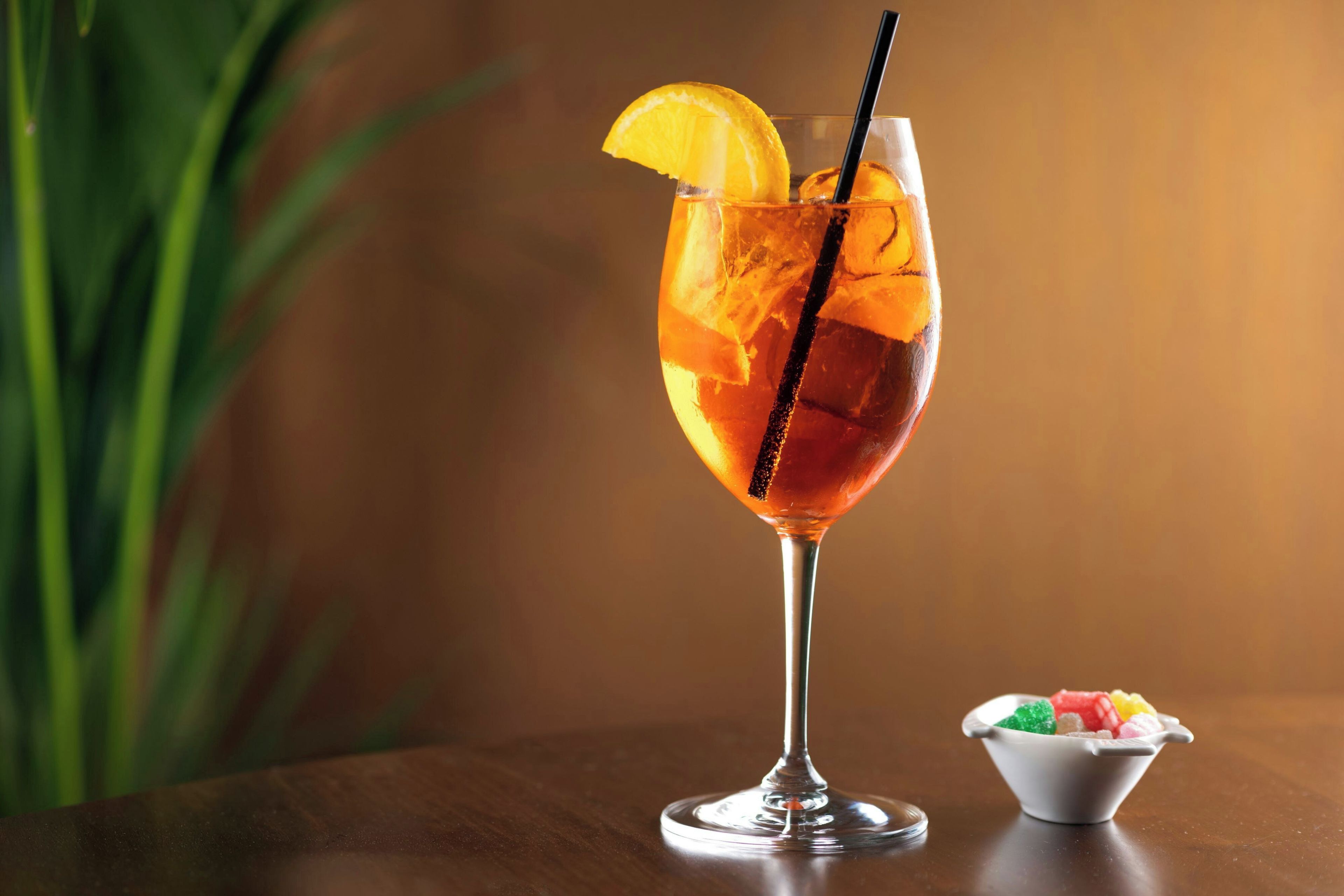 A cocktail glass with a slice of orange and a straw, placed on a wooden table.