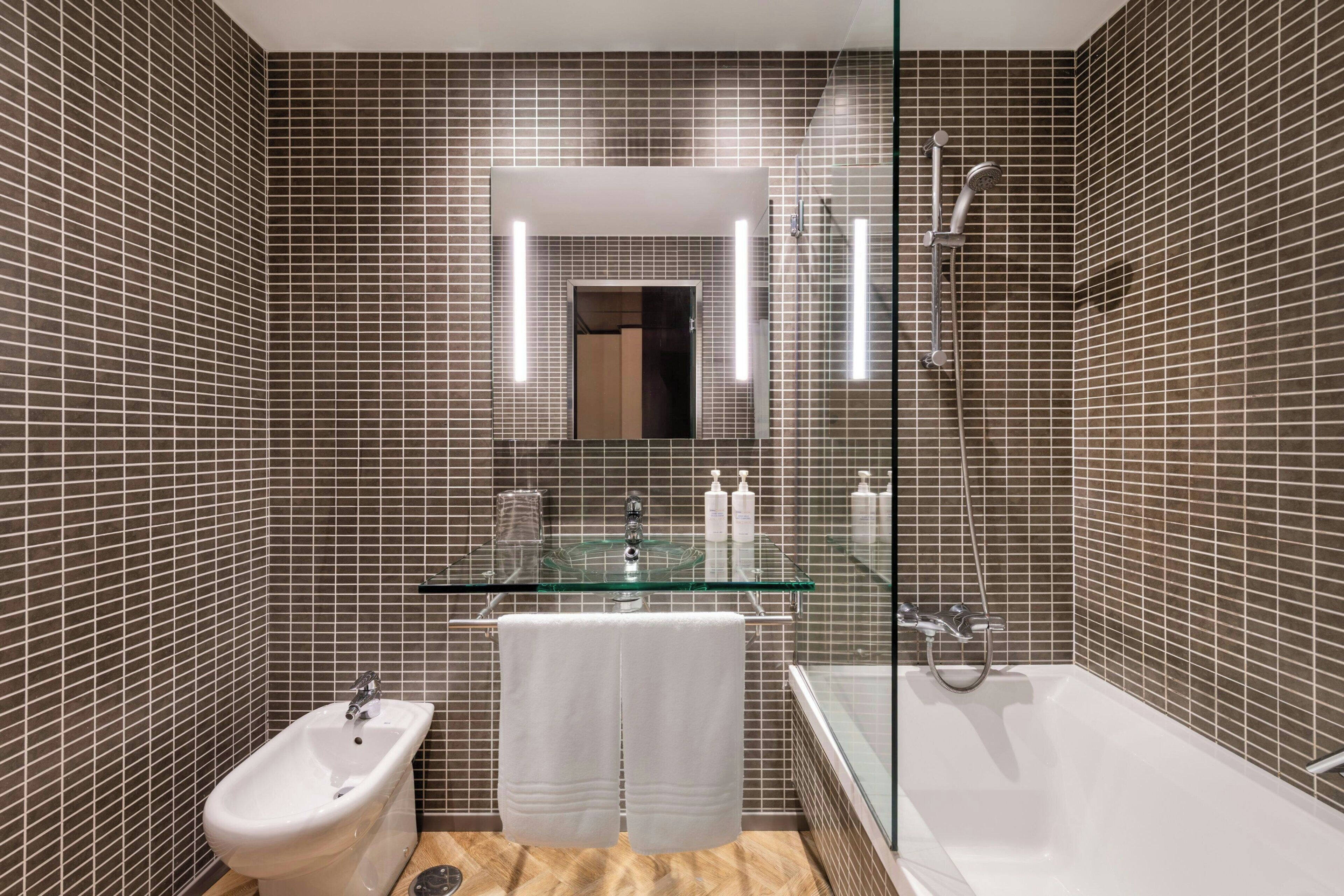 A modern bathroom with a bidet, a glass sink, and a bathtub.