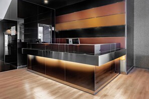 A reception desk with a modern design, featuring a black and metallic color scheme and a flat-screen monitor. - AC Hotel Palacio Universal by Marriott (Vigo)