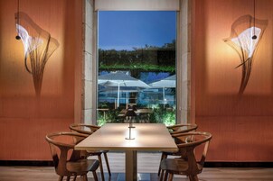 A dining area with a table and chairs, a view of an outdoor seating area with umbrellas, and wall-mounted light fixtures.