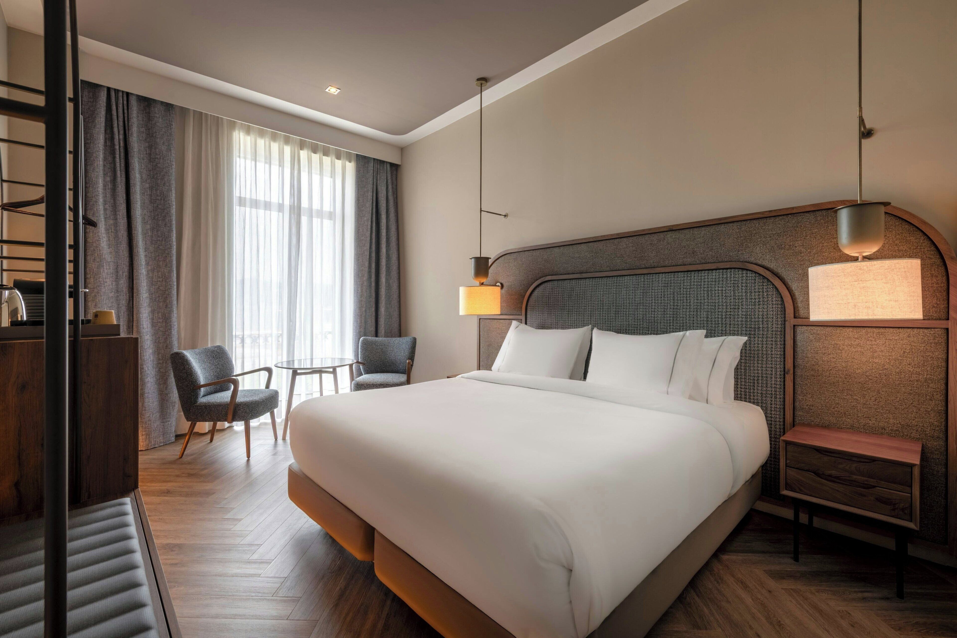 Une chambre d’hôtel avec un grand lit, deux fauteuils, un bureau et une lampe.