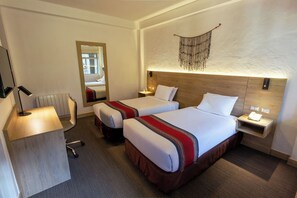 Habitación de hotel con dos camas, un escritorio, un espejo y un teléfono en la pared.