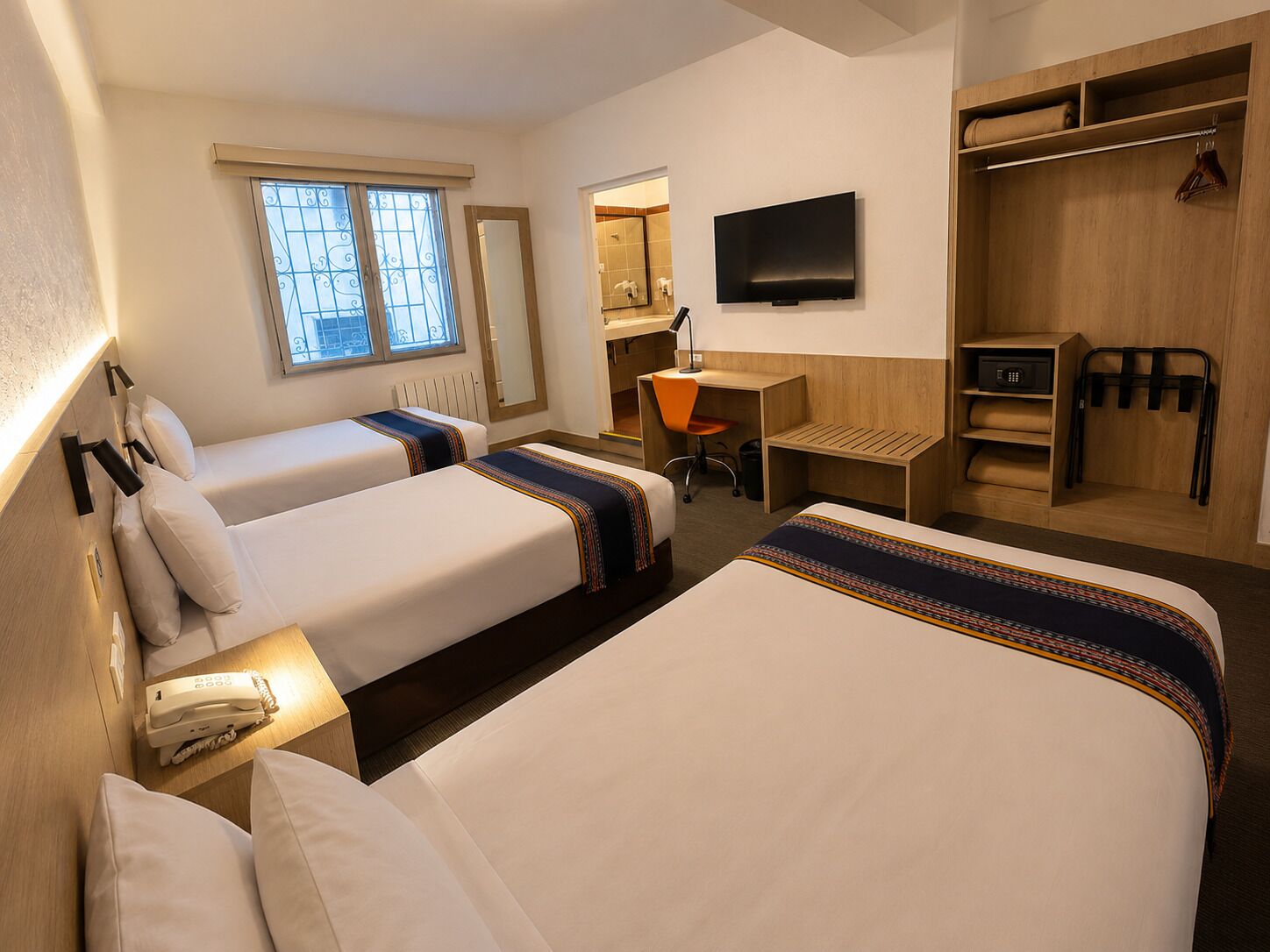 A hotel room with two beds, a desk, a chair, a TV, and a wardrobe.