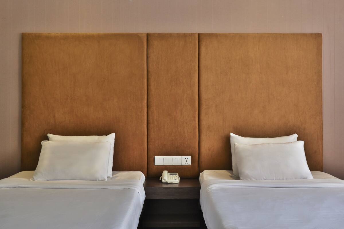 Ein Hotelzimmer mit zwei Betten, einem Holz-Kopfteil, einem Nachttisch mit Telefon und einer Steckdose.
