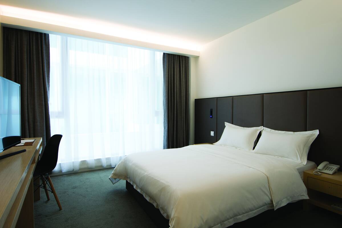 Habitación de hotel con una cama grande, un escritorio con silla, una mesita de noche con teléfono y un amplio ventanal con cortinas.