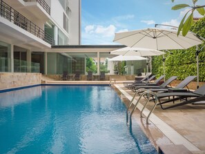 A modern pool area with a clear blue pool, sun loungers, and umbrellas. - Taiming Hotel (Phnom Penh)
