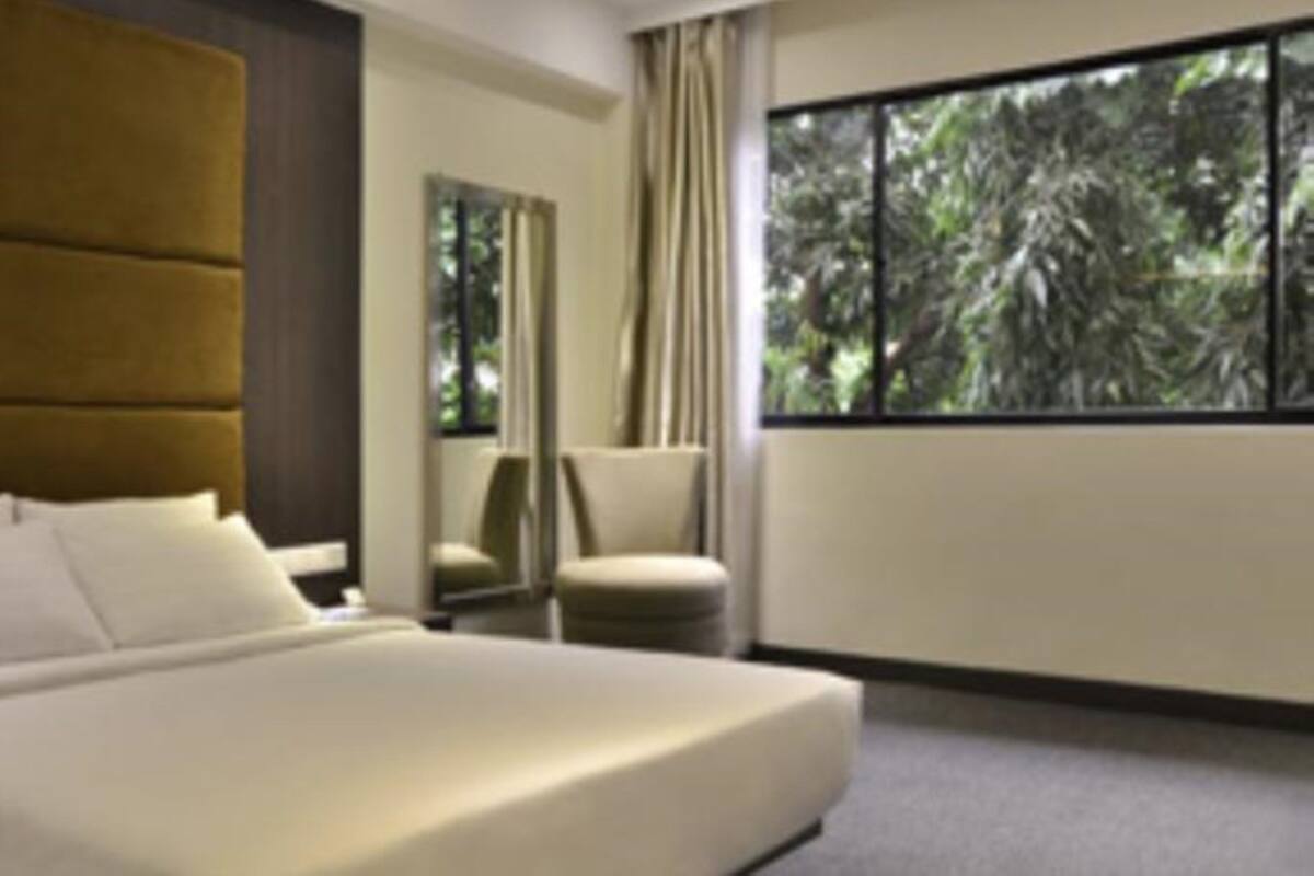 Habitación de hotel moderna con una cama grande, un espacio de descanso con una silla y un gran ventanal con vistas a árboles.
