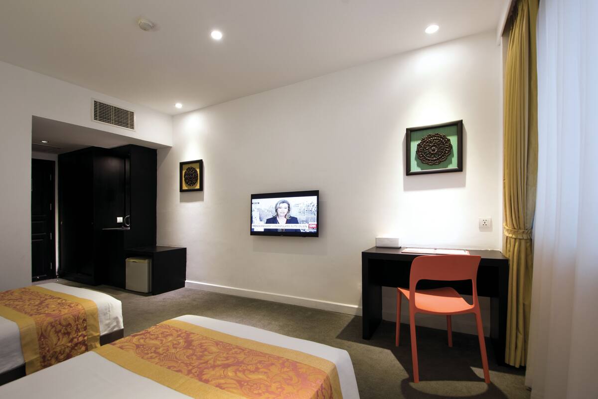 Ein Hotelzimmer mit zwei Betten, einem Schreibtisch, einem Sessel, einem Fernseher und einem kleinen Kühlschrank.