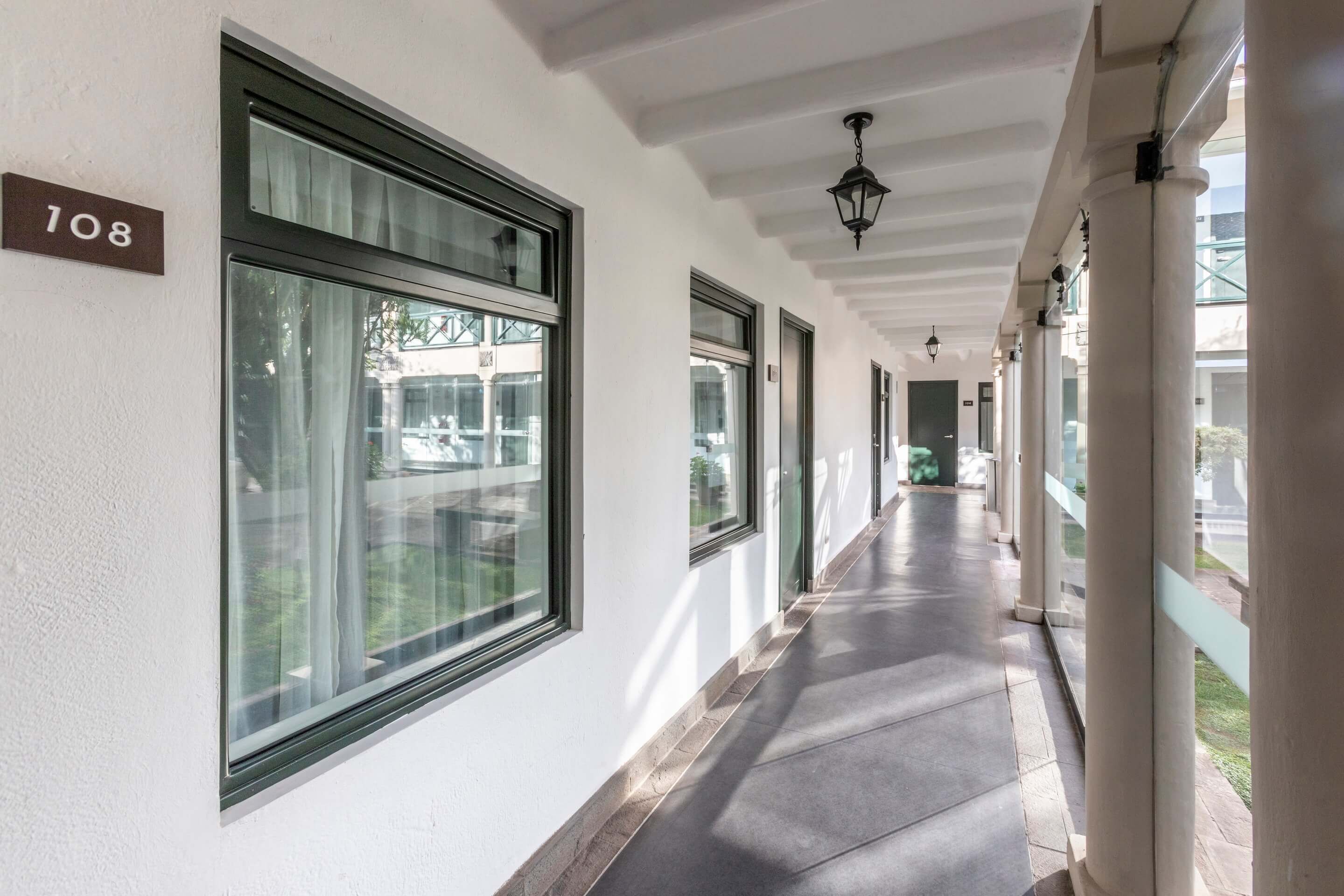 A corridor with large windows, a number sign '108', and a hanging light fixture.