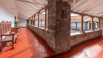 A covered corridor with stone pillars, wooden benches, and a tiled floor.