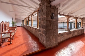 A covered corridor with stone pillars, wooden benches, and a tiled floor.