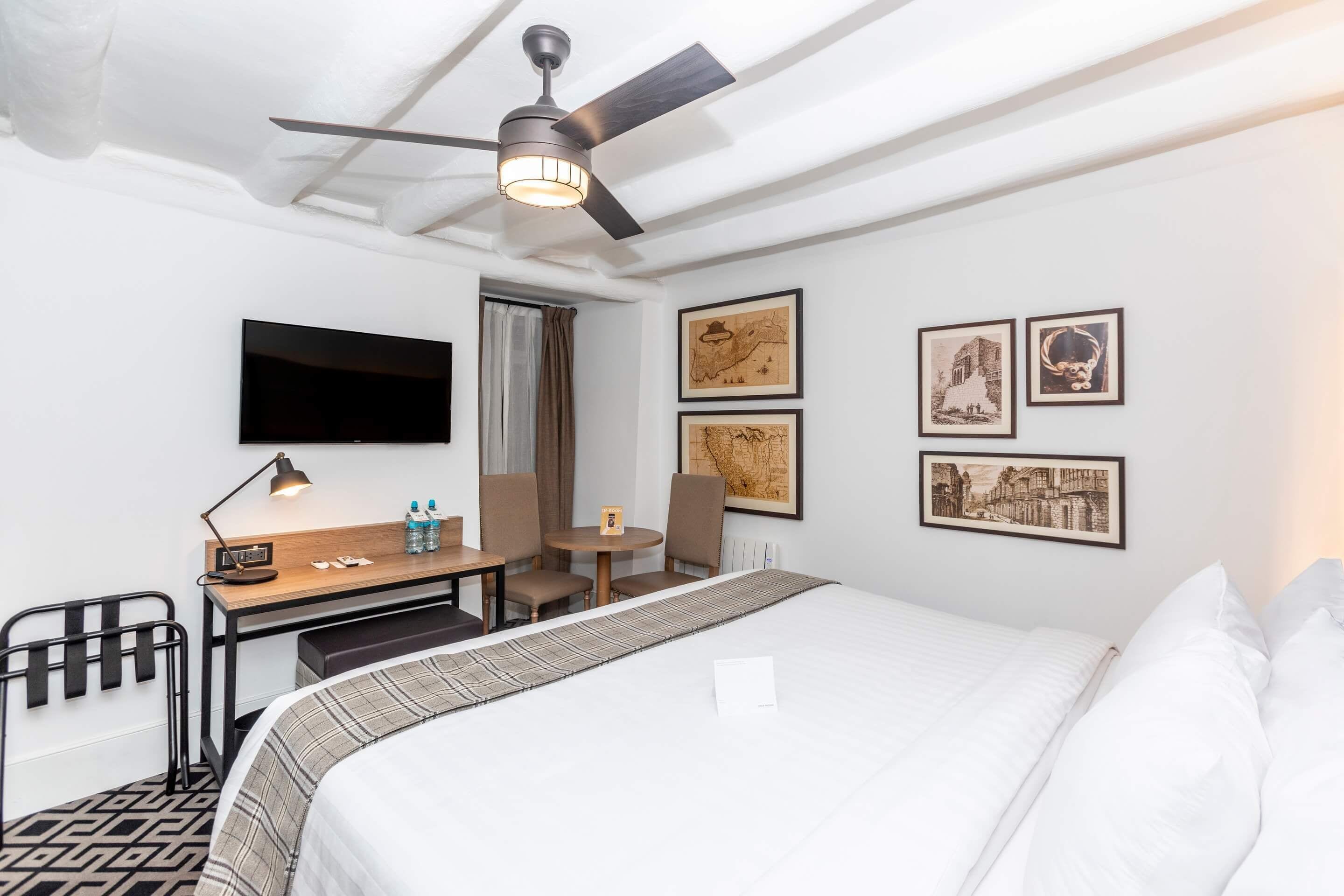 Une chambre d’hôtel équipée d’un lit, d’un bureau, d’une chaise et d’un ventilateur de plafond.