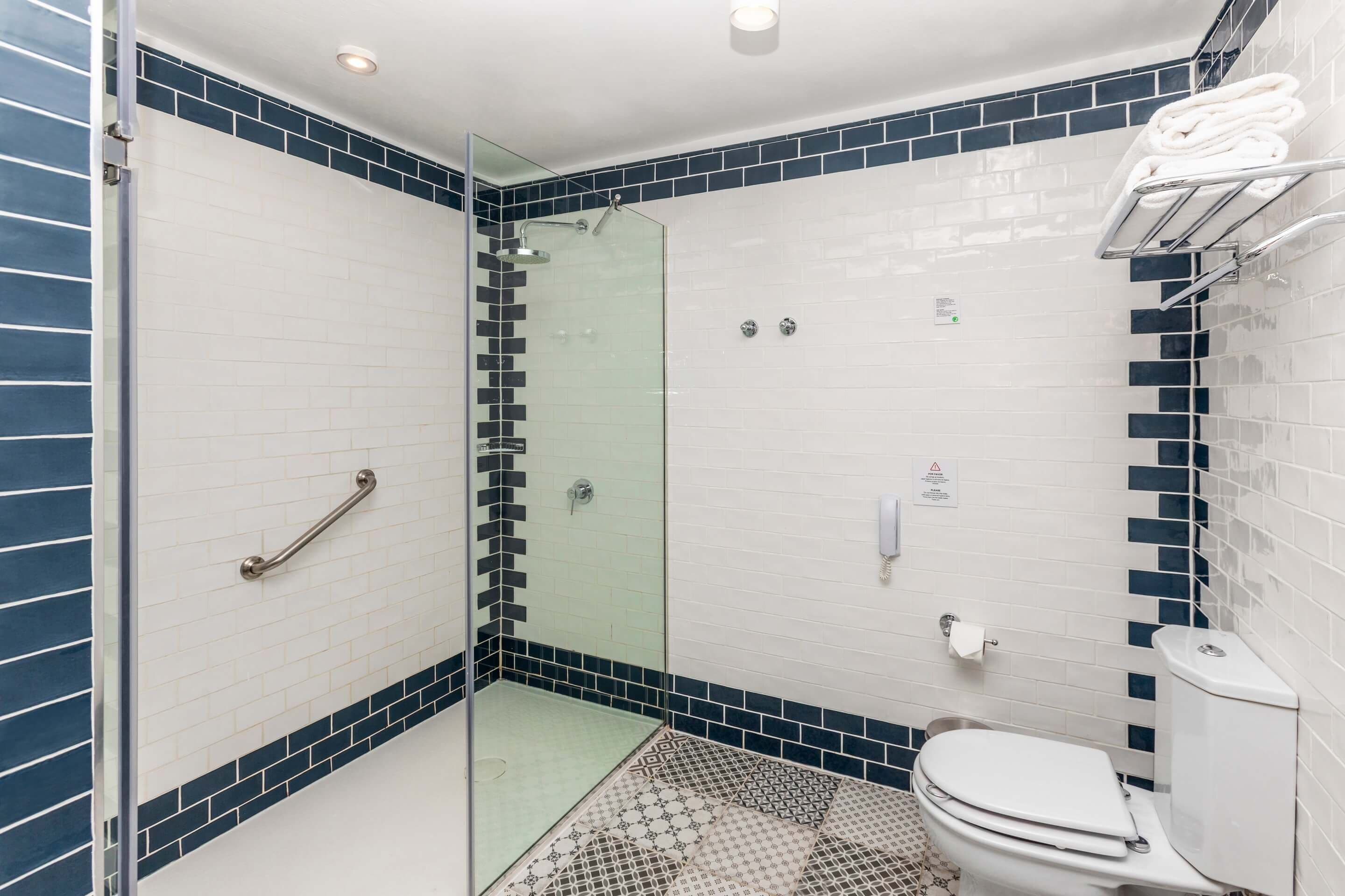 Un baño moderno con ducha de vidrio, paredes de azulejos blancos y piso estampado.