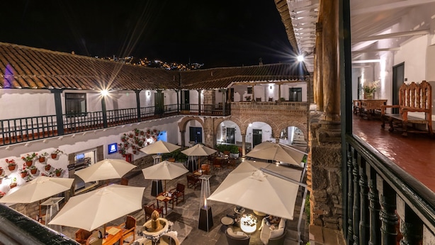 An outdoor courtyard with multiple tables and chairs, umbrellas, and potted plants. - Casa Andina Premium Cusco (Cusco)