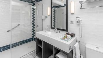 Un baño moderno con ducha de vidrio, lavamanos blanco con tocador y un espejo grande.