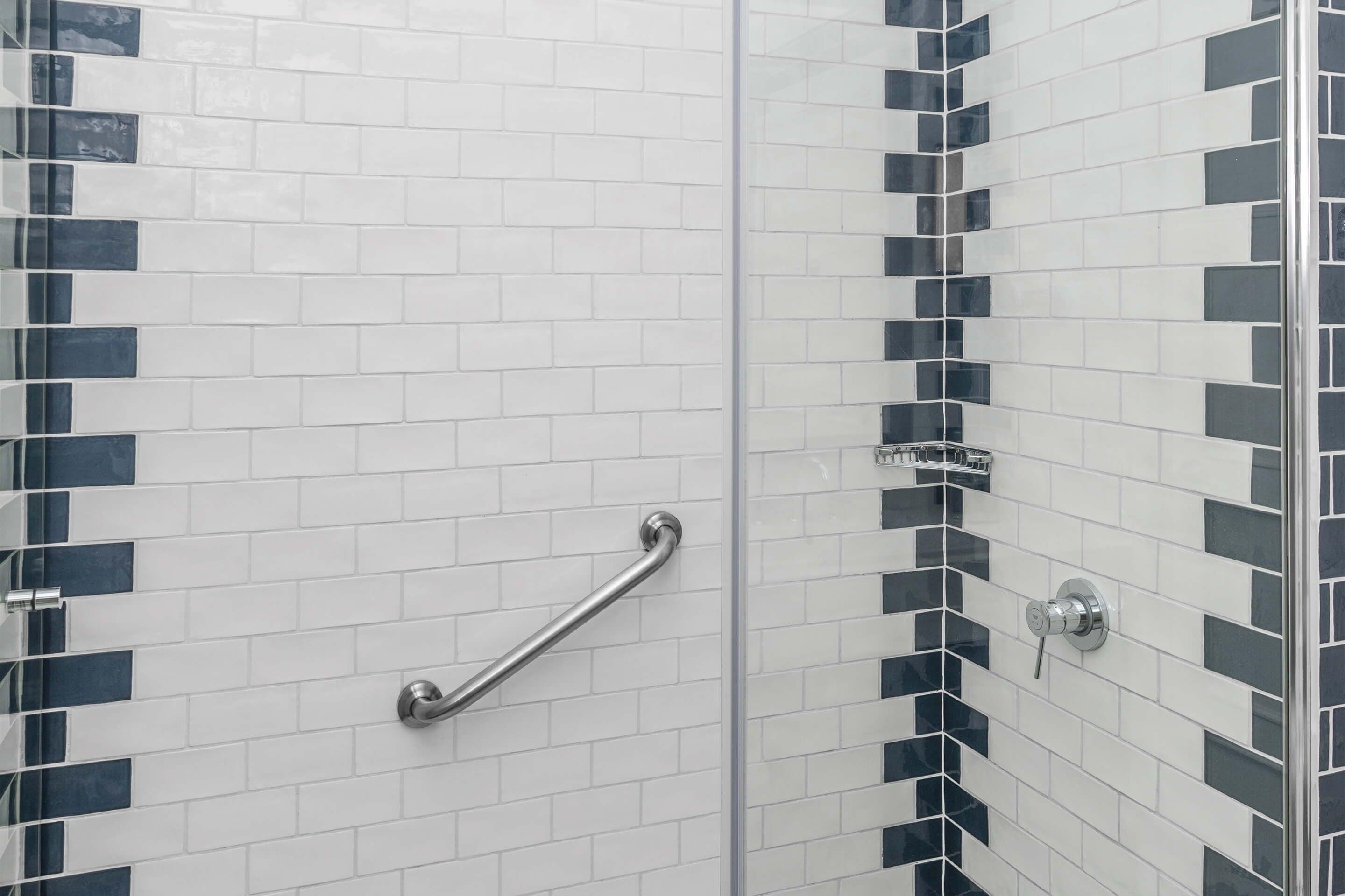 Une salle de bain avec des carreaux noirs et blancs, une douche en verre et une barre d’appui.