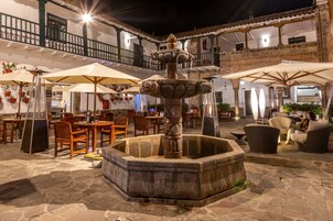 Un patio con una fuente de piedra, asientos al aire libre y un edificio con balcones.