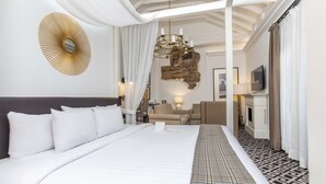 A hotel room with a large bed, a chandelier, a stone wall, a sofa, and a television. - Casa Andina Premium Cusco (Cusco)