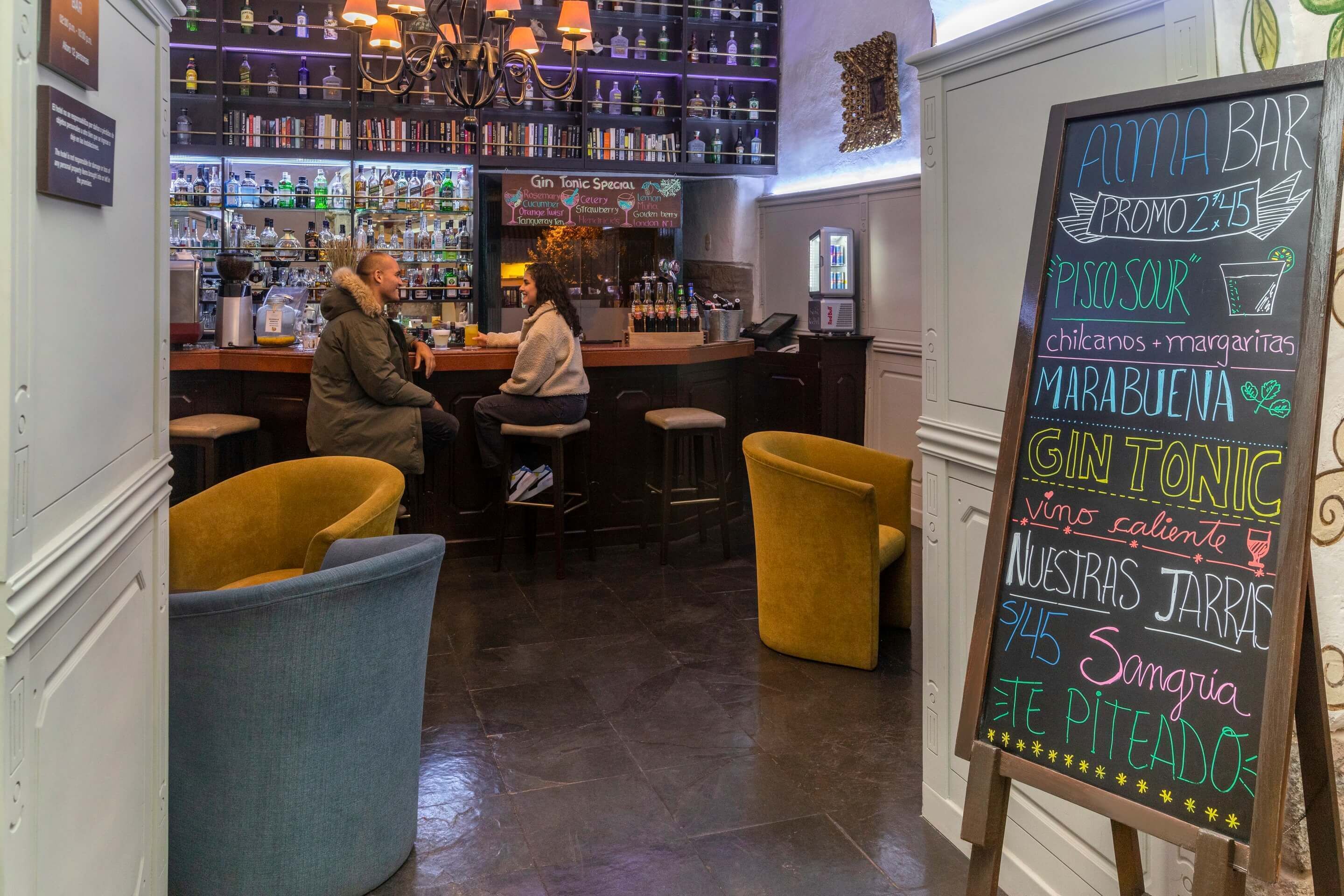 A bar area with a chalkboard menu, bar stools, and shelves with bottles.
