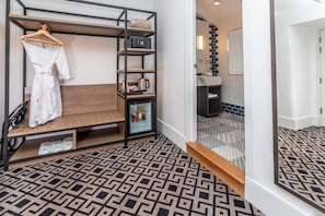 A hotel room with a wooden bench, a robe hanging on a rack, a microwave, and a small refrigerator.