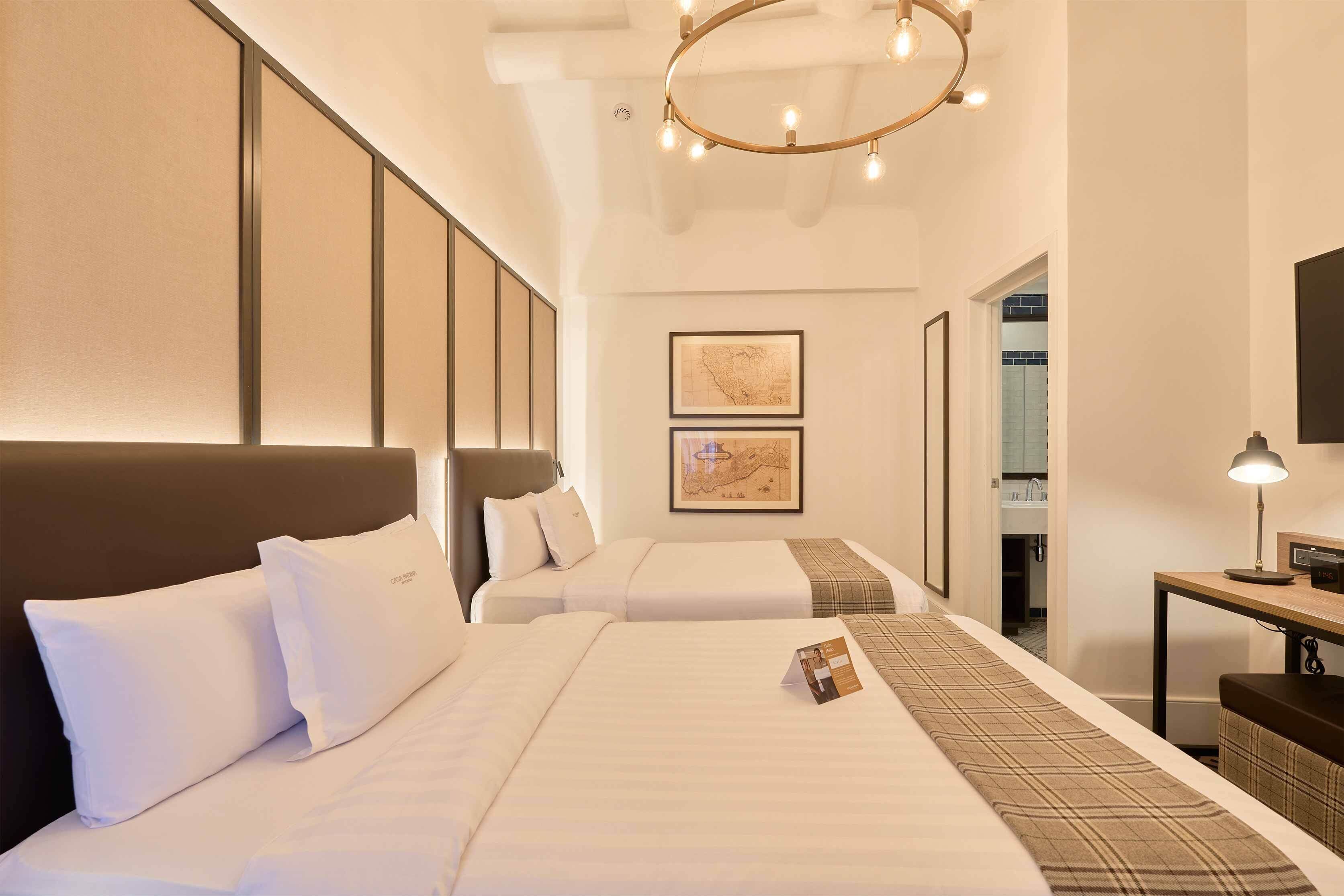 Quarto de hotel com duas camas, uma escrivaninha, um espelho e um mapa na parede.