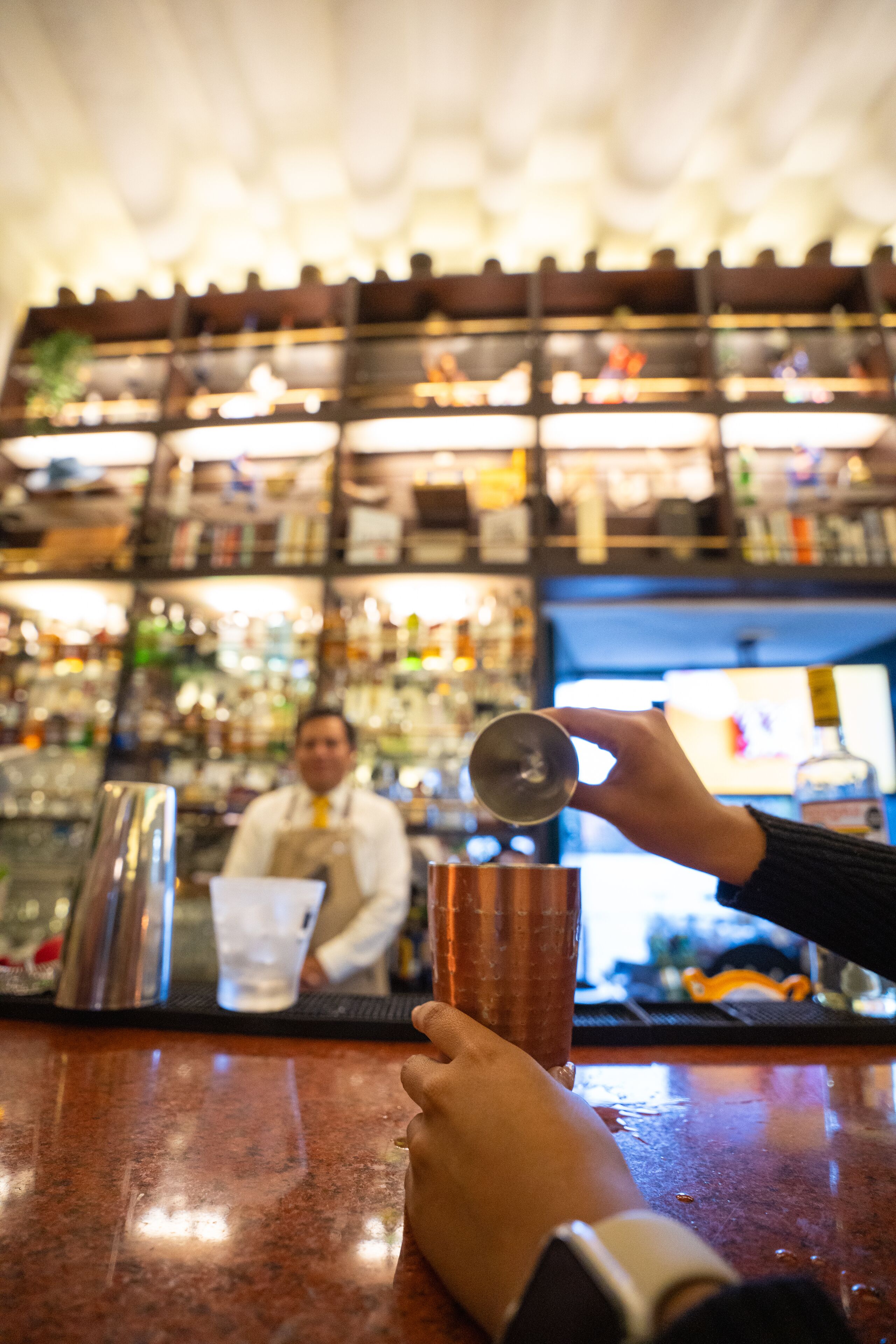 A bar counter with a person pouring a drink into a glass.