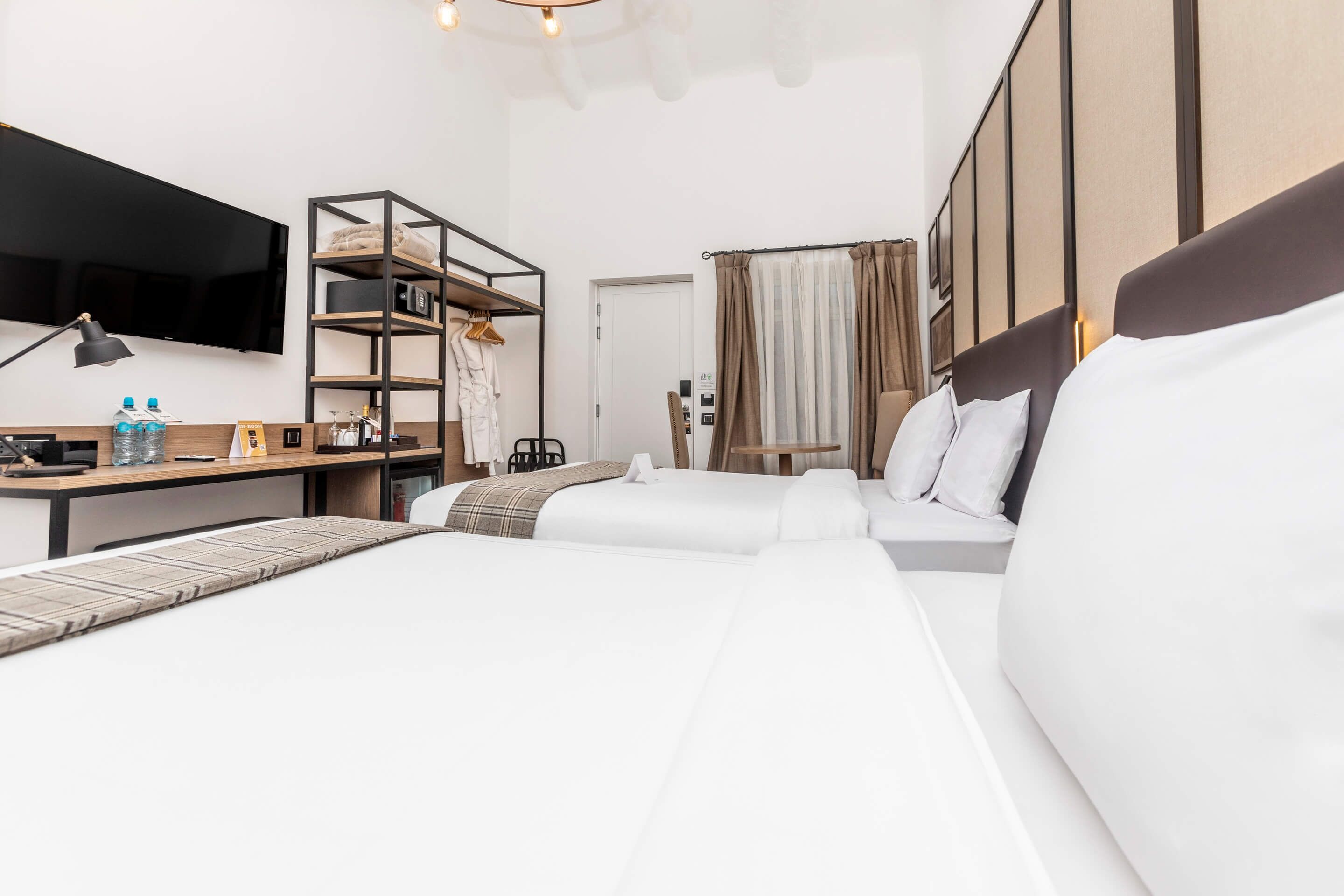 A modern hotel room with a large bed, a desk with a lamp, a TV mounted on the wall, and a wardrobe.