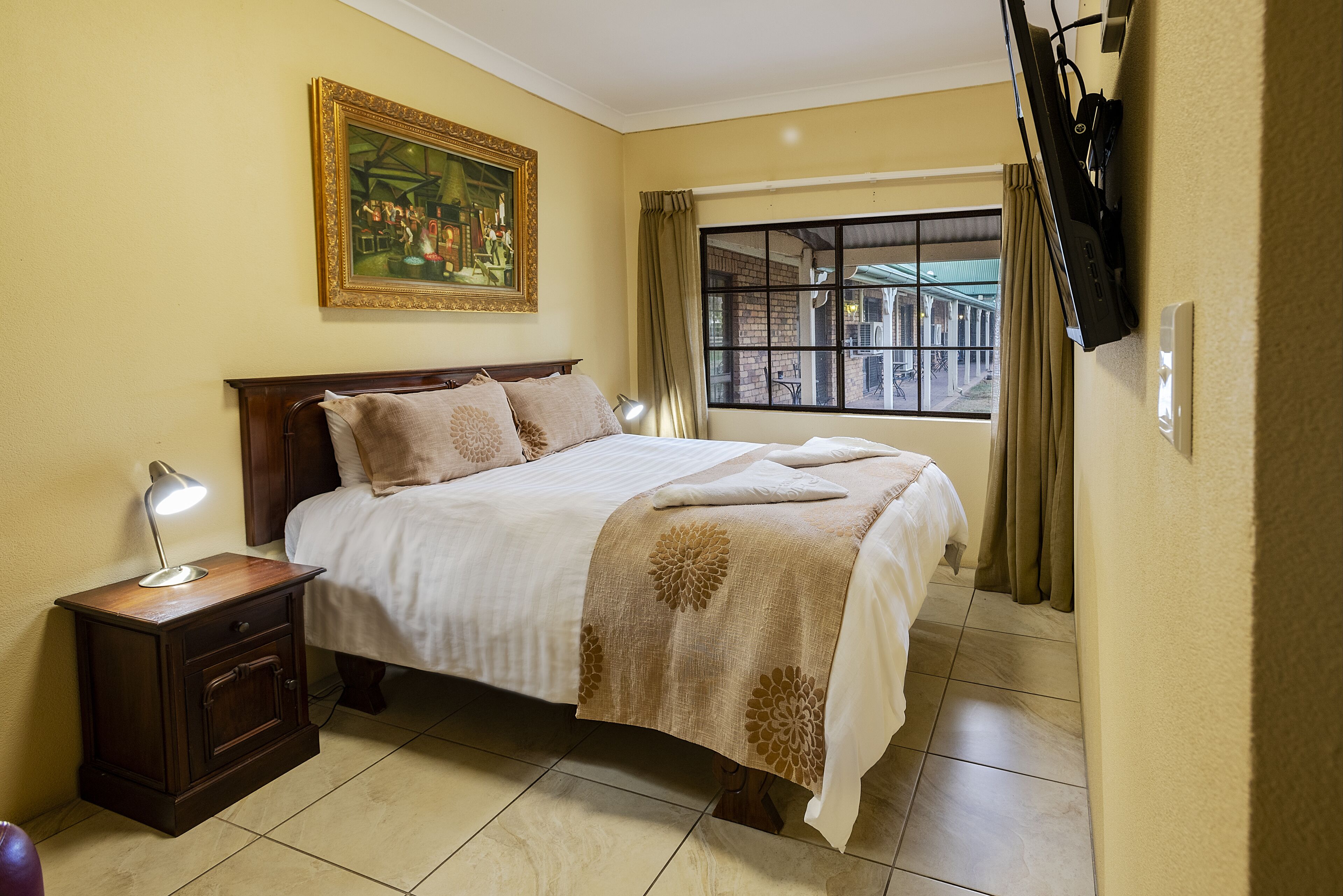 A neatly arranged bedroom with a bed, bedside table, lamp, and a large window with curtains.